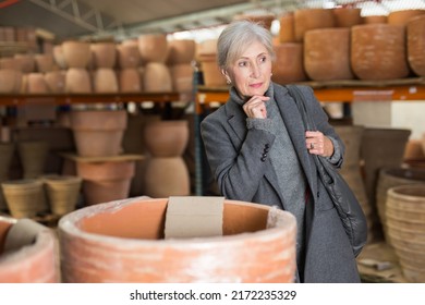 Senior Woman Choosing Earthenware Pot In Crockery Store.