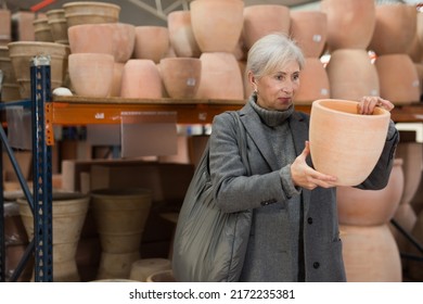 Senior Woman Choosing Earthenware Pot In Crockery Store.