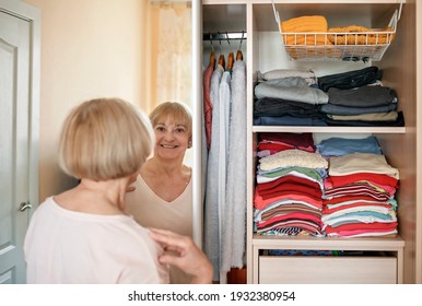 Senior Woman Choosing Outfit From Wardrobe Closet With Clothes And Home Stuff. Cleaning, Organizing And Order In The Closet