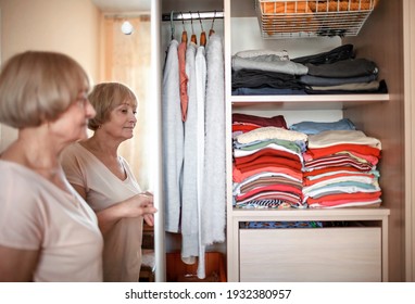 Senior Woman Choosing Outfit From Wardrobe Closet With Clothes And Home Stuff. Cleaning, Organizing And Order In The Closet