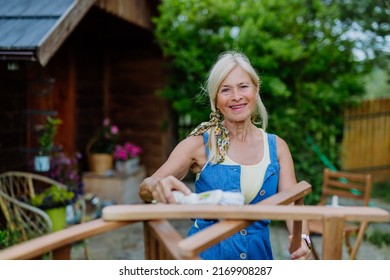 Senior Woman Cleaning Garden Furniture And Getting The Garden Ready For Summer