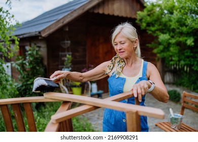 Senior Woman Cleaning Garden Furniture And Getting The Garden Ready For Summer