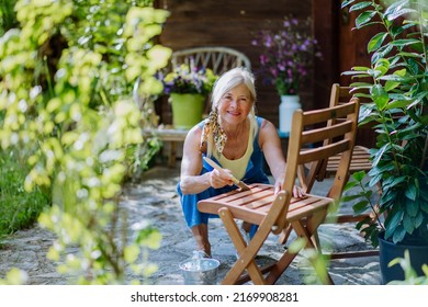 Senior Woman Cleaning And Renovating Garden Furniture And Getting The Garden Ready For Summer