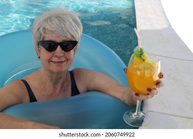 Senior woman with cocktail and sunglasses in hotel swimming pool