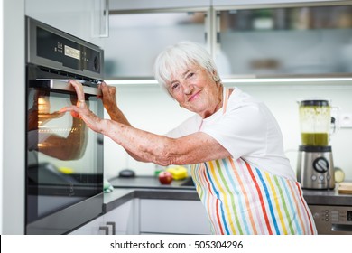 Senior Woman Cooking In The Kitchen - Eating And Cooking Healthy For Her Family; Putting Some Potates In The Oven, Enjoying Active Retirement (shallow DOF; Color Toned Image)