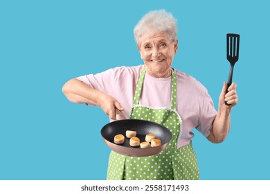 Senior woman with cottage cheese pancakes in frying pan on blue background - Powered by Shutterstock