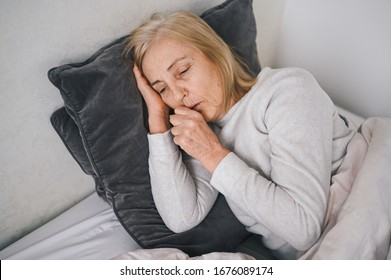 Senior Woman Coughing In Fist Sick Of Coronavirus Viral Infection Spreading Corona Virus Covering Mouth And Nose. Painful Cough Ill Elderly Patient Lying In Bed At Home Quarantine. First Symptoms 