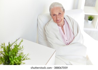 Senior Woman Covered With Blanket Sitting On Sofa