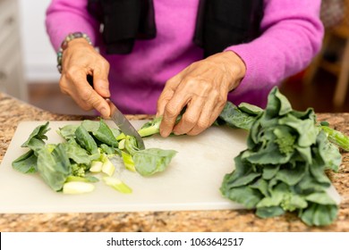 Senior Woman Cutting Kale On Chopping Board In Kitchen