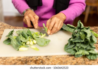 Senior Woman Cutting Kale On Chopping Board In Kitchen