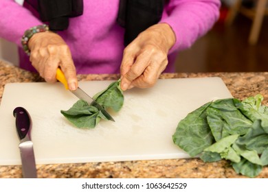 Senior Woman Cutting Kale On Chopping Board In Kitchen