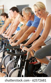 Senior Woman Cycling In Class In Gym