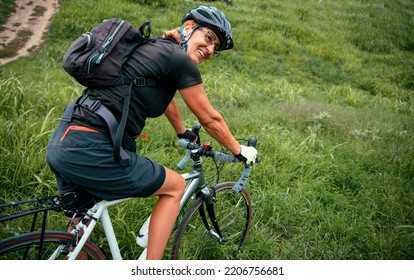 Senior Woman Cyclist In Black Sportswear And Helmet Riding Bicycle Outdoors In Green Nature. Copy Space