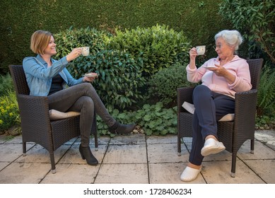 Senior Woman And Daughter With Face Masks Having Coffee With Safety Disctance