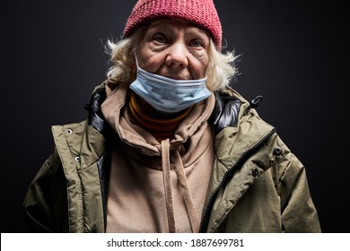 Senior Woman In Dirty Wear And Medical Mask Isolated On Black Background, Homeless Female Is Suffering From Hunger And Cold, In Desperation