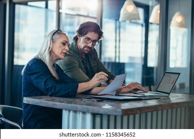Senior woman discussing work with male colleague. Two business associates working together in office and talking over a business report. - Shutterstock ID 1158345652