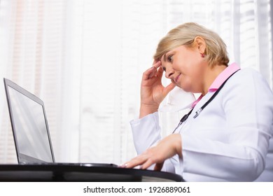 Senior Woman Doctor At The Computer In Her Office Holding Her Head. Fatigue. Stress. Work Days.