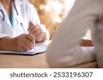 Senior woman doctor consults with young patient in modern medical office, doctor explaining and diagnosis with patient about health and treatment while writing on notes, medical and insurance.