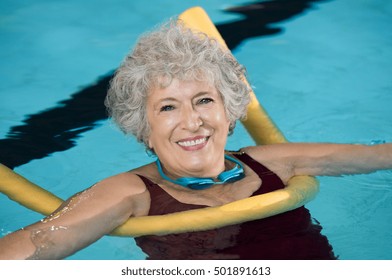 Senior Woman Doing Aqua Fitness With Swim Noodles. Mature Woman Doing Water Aerobics With A Yellow Noodle. Old Woman In Swimming Pool Doing Aquarobic And Rehabilitation Exercise.