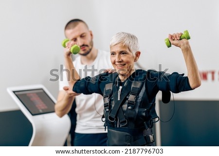 Senior woman is doing EMS training with personal trainer in the gym.