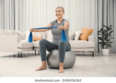 Senior woman doing exercise with elastic resistance band on fitness ball at home - Powered by Shutterstock