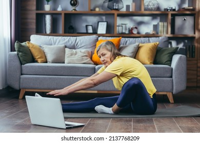 Senior Woman Doing Fitness, Sitting On The Floor At Home, Using Laptop For Online Sports Group Activities