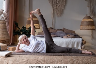 Senior Woman Doing Fitness Workout, Exercise Stretching Legs, Anantasana Or Side Reclining Leg Lift Yoga Pose At Home