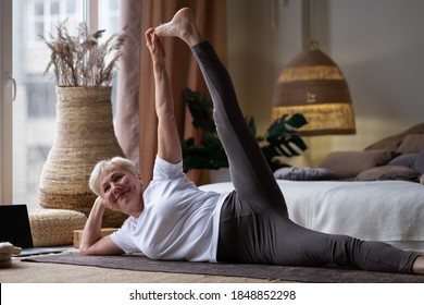 Senior Woman Doing Fitness Workout, Exercise Stretching Legs, Anantasana Or Side Reclining Leg Lift Yoga Pose At Home