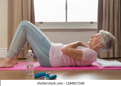 Senior Woman Doing Sit Ups On Yoga Mat At Home. Fit Healthy Old Woman Doing Abdomen Crunches At Home. Elderly Woman Keeping Fit By Exercising For Staying Healthy.