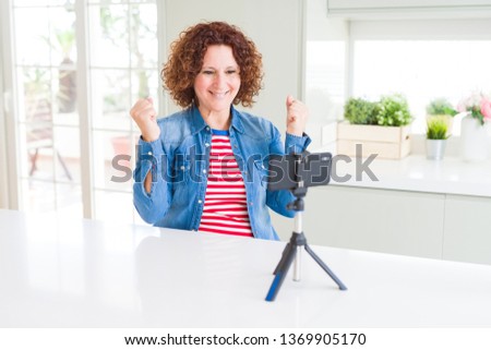 Senior woman doing video chat using smartphone camera celebrating surprised and amazed for success with arms raised and open eyes. Winner concept.