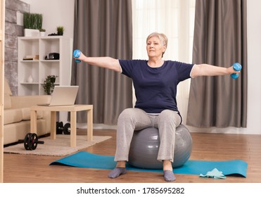 Senior woman doing warm up exercise at home. Old person pensioner online internet exercise training at home sport activity with dumbbell, resistance band, swiss ball at elderly retirement age - Powered by Shutterstock