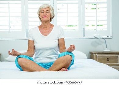 Senior Woman Doing Yoga Against Window On Bed At Home