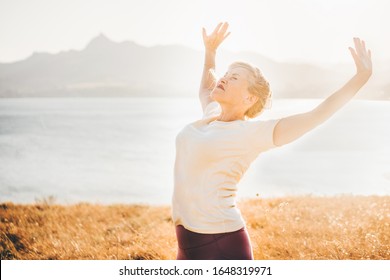 Senior woman doing yoga exercises at the sea and mountain on the background at the sunset. Feeling the harmony. Concept of calm and meditation. - Powered by Shutterstock