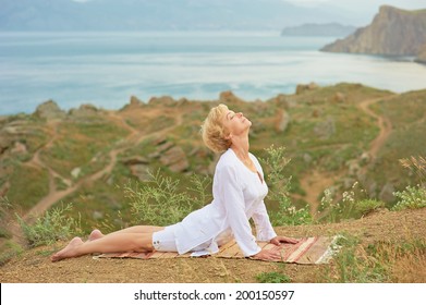 Senior woman doing yoga exercises with beautiful mountain view on the background