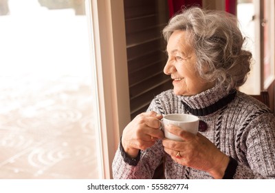 Senior Woman Drinking Coffee And Looking Through Window