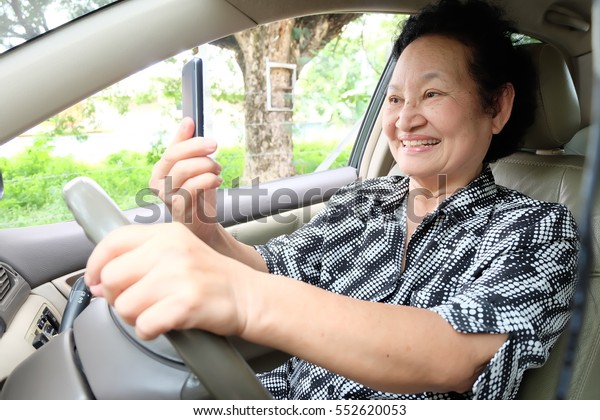 Senior woman driving car\
and cellphone