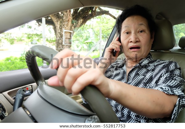 Senior woman driving car\
and cellphone