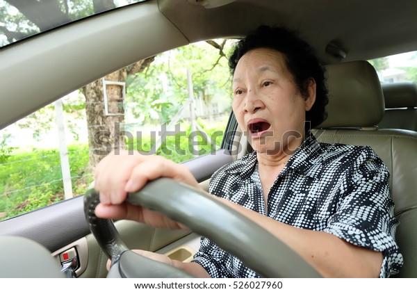 Senior woman\
driving car with scared\
expression
