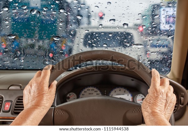 Senior\
woman driving a car slowly in city ,rainy\
season