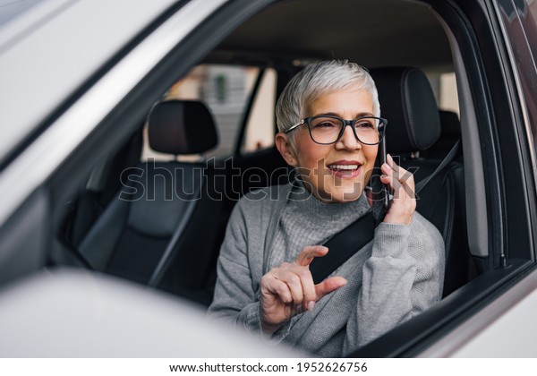 Senior woman driving a car and talking on\
smart phone. Asking for a\
direction.