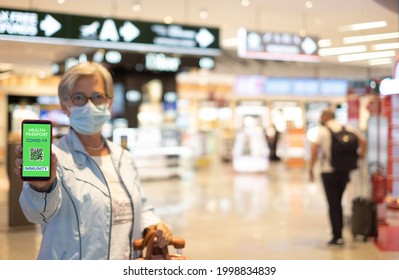 Senior woman in duty free area in airport waiting for boarding, showing mobile app for people vaccinated of covid-19. Immunity passport for travel - Powered by Shutterstock