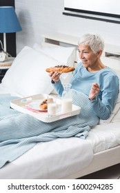 Senior Woman Eating Breakfast In Bed. She Watching Tv And Eat Chocolate Croissant