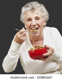 Senior Woman Eating Cereals Out Of A Red Bowl Against A Black Background