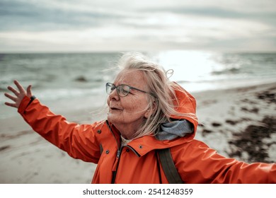 Senior woman enjoying freedom on windy beach with arms outstretched - Powered by Shutterstock