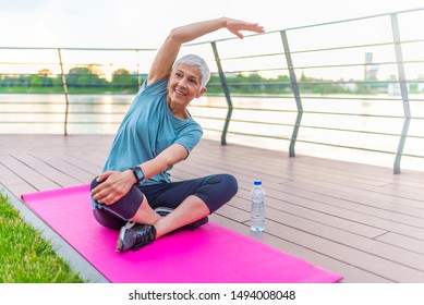 Senior Woman Enjoying Nature During A Breathing Exercise. Portrait Of A Fitness Woman Stretching Arms And Looking Away Outdoor. Beautiful Senior Woman Exercise. Yoga Woman In Park