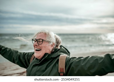 Senior woman enjoying a windy day at the beach with arms outstretched - Powered by Shutterstock