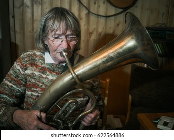 Senior woman enjoys playing on a horn in a rustic living room - retro style