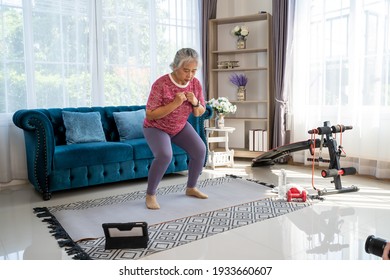 Senior Woman Exercise With Squat Pose, She Watch Laptop For Training Exercise Online In Living Room During Quarantine