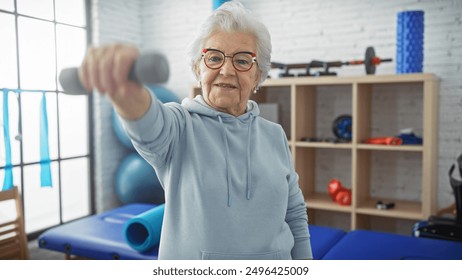 A senior woman exercises with dumbbells in a physiotherapy clinic's rehab room, showcasing healthcare and fitness. - Powered by Shutterstock