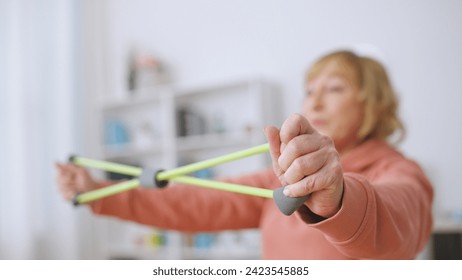 A senior woman exercises with a stretching band, committed to an active lifestyle and fitness at home - Powered by Shutterstock